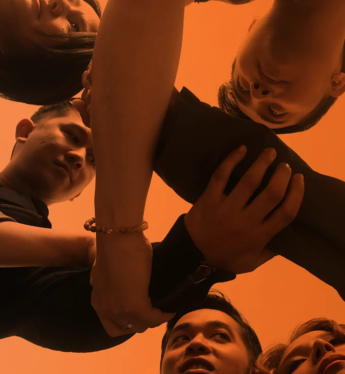 The five members of Pinopela joining hands in a huddle, photographed from below