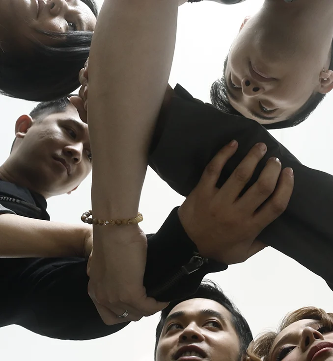 Pinopela joining hands in a huddle, photographed from below in natural light